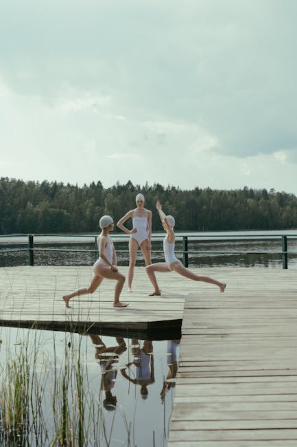 Woman practicing yoga outdoors on a wooden deck by the water at sunrise.